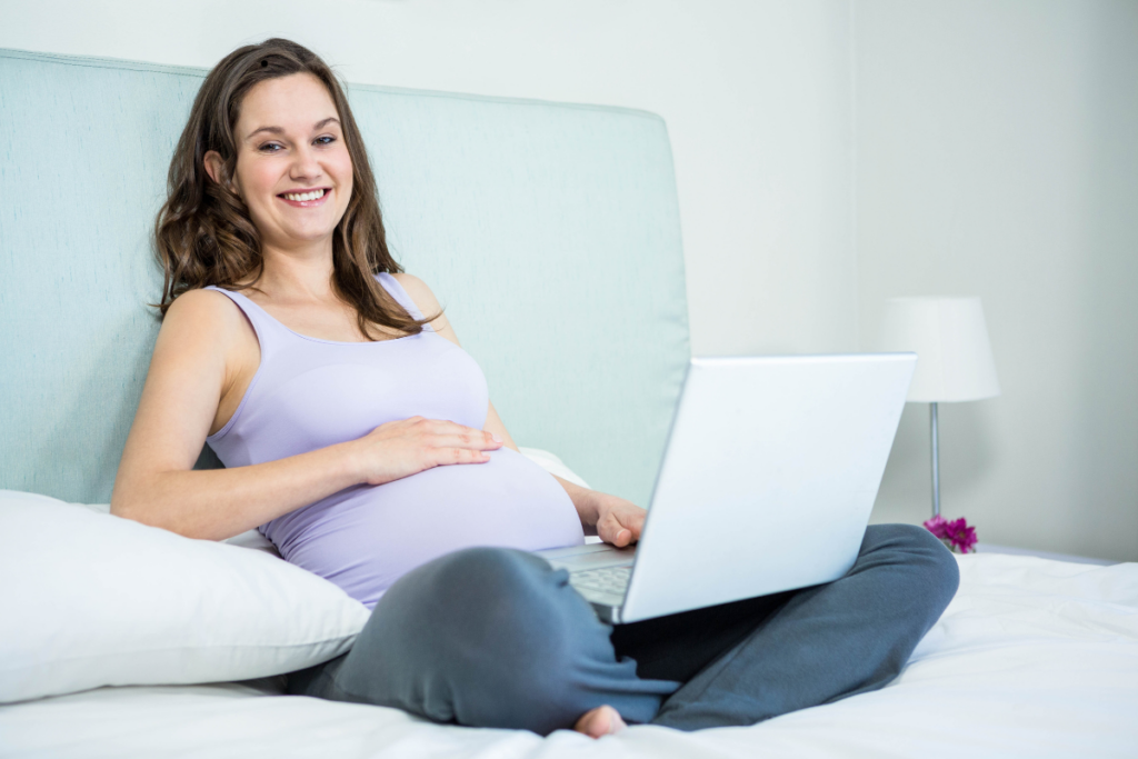 Boldog várandós nő kapcsolódik laptopon a Világra Hívók online közösségéhez